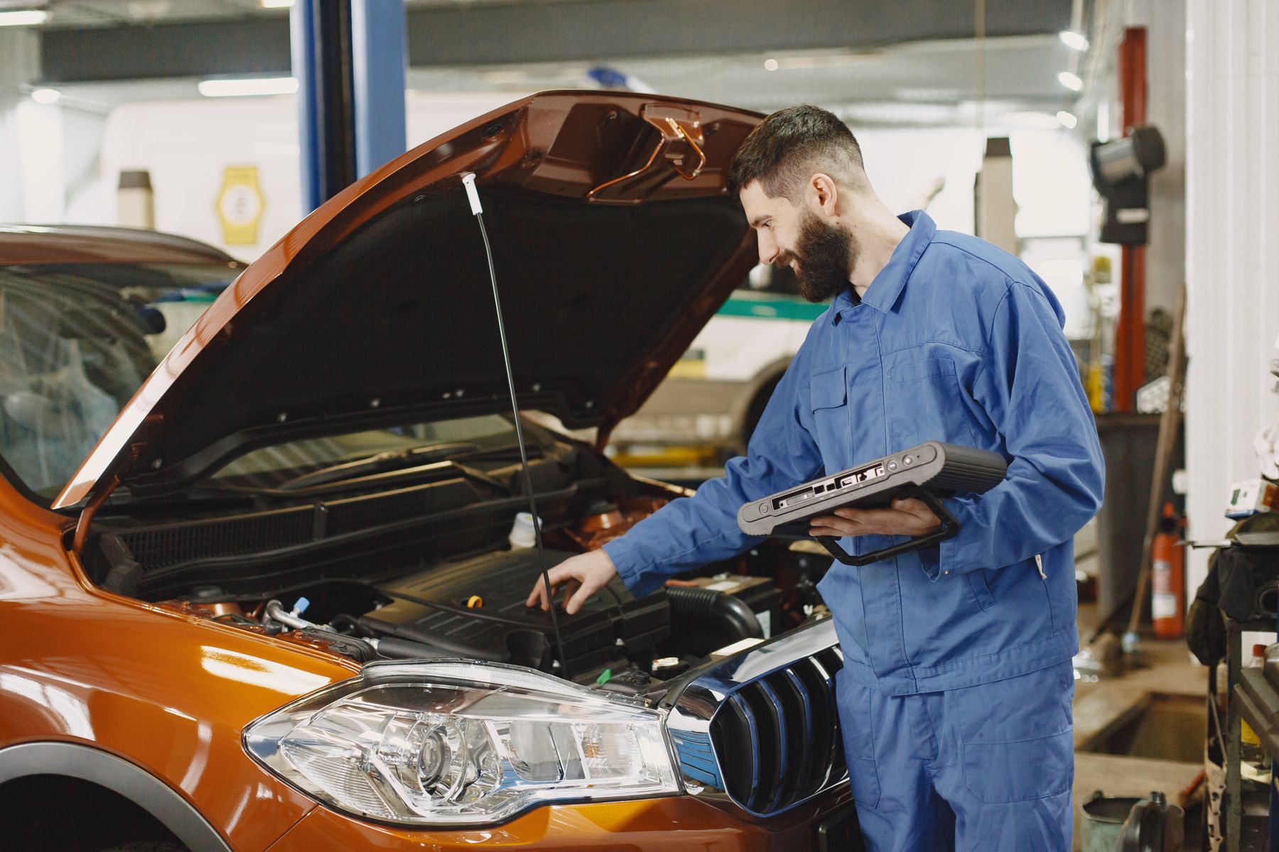 Technicien en agence partenaire, valise de diagnostic en main, devant le capot ouvert d'une voiture