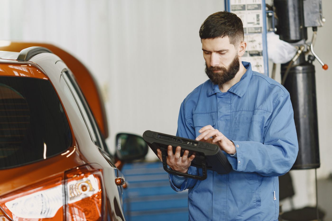 Technicien d'une agence automobile consultant une valise de diagnostic à côté d'un véhicule